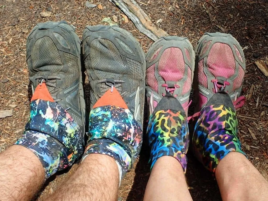 Two pairs of feet in trail running shoes and colorful gaiters