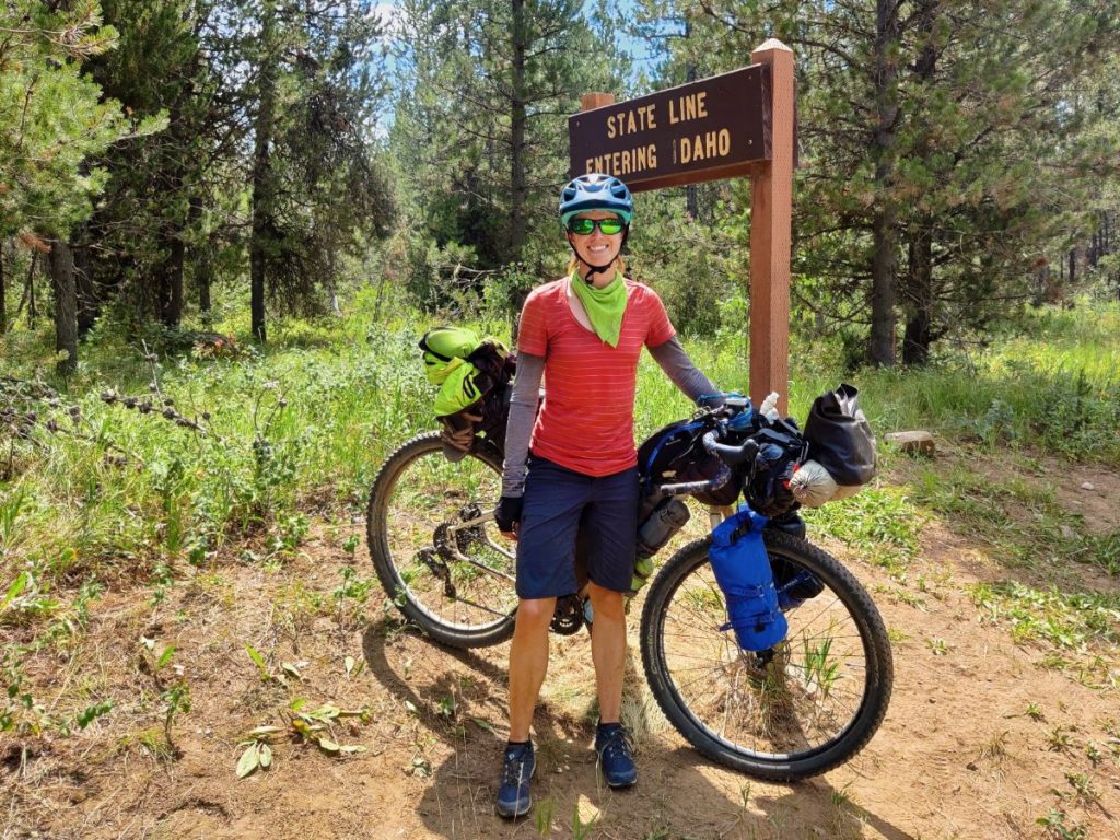 Woman with bikepacking bike in front of Idaho state line sign on the Great Divide