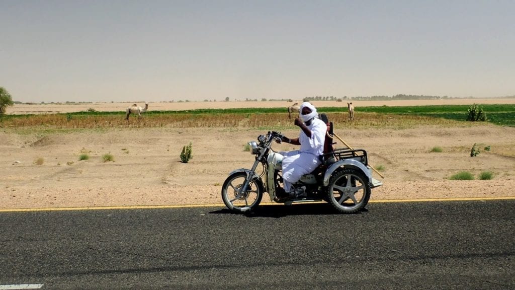 Friendly Sudanese man in white robes waves from motorbike