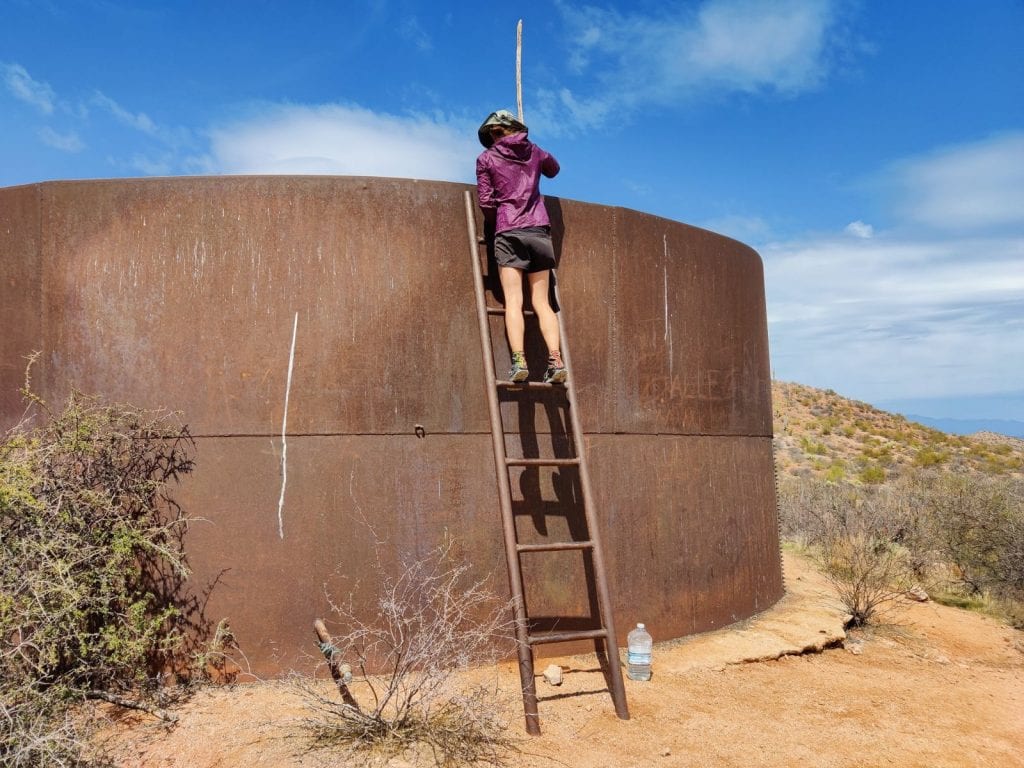 Backpacker climbs ladder to get water from tank in the desert