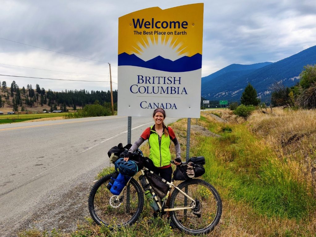 Woman and her loaded bike in front of Welcome to British Columbia sign