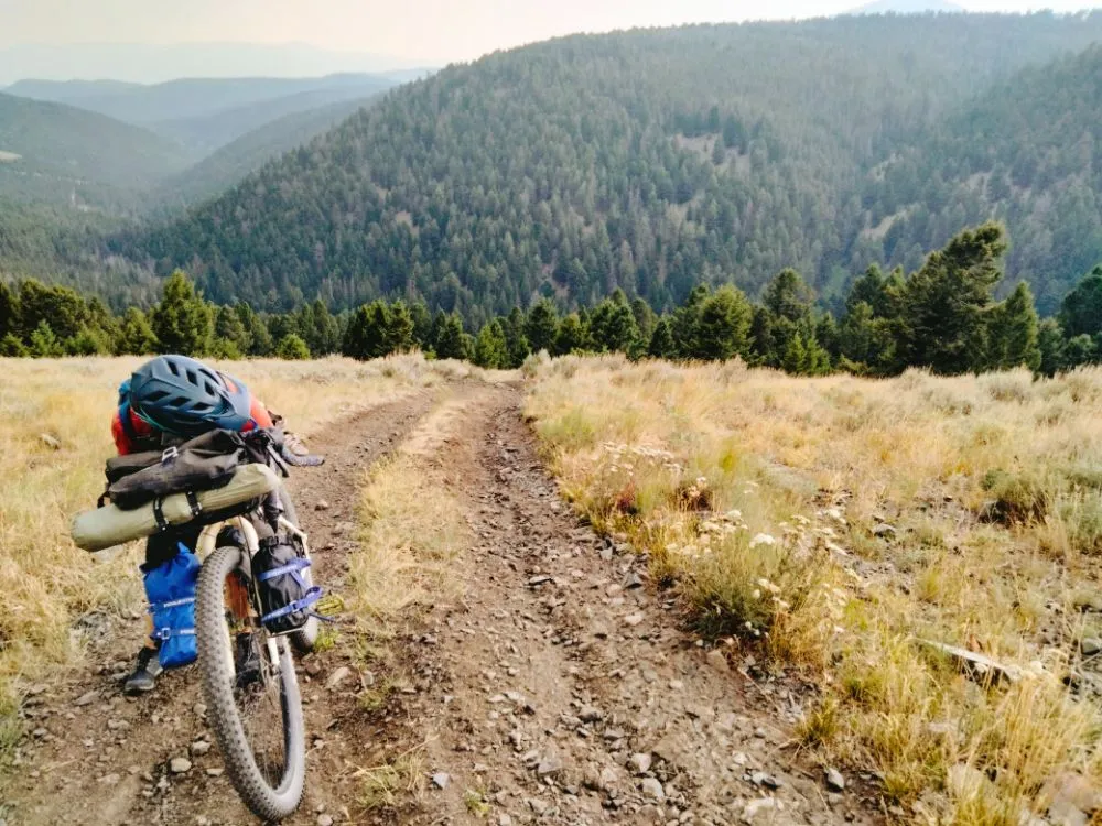 Bikepacker stops to rest while pushing her bike up very steep hill